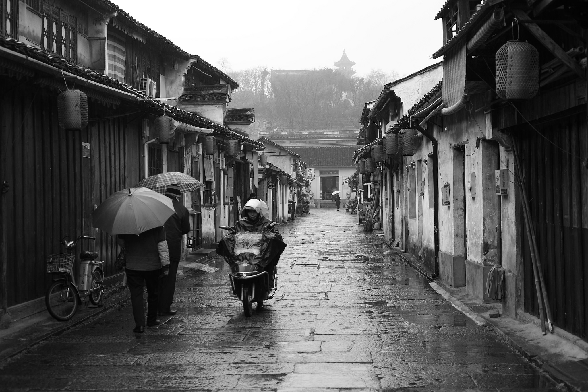 雨中的绍兴老街，行人撑伞，电动车沿石板巷驶来